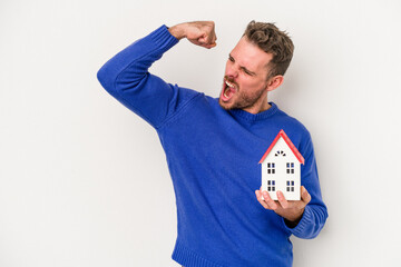 Young caucasian man holding a little house isolated on white background raising fist after a victory, winner concept.