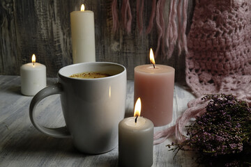 Pink knitted scarf, burning candles and a cup with coffee on a wooden table, hygge style