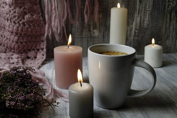 Obraz na płótnie Canvas Knitted scarf, burning candles and a cup of tea on a wooden table, hygge style