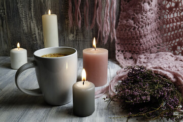 Pink knitted scarf, burning candles and a cup with coffee on a wooden table, hygge style