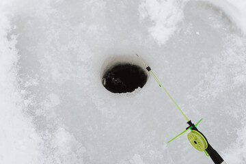 Winter fishing hobby concept. Top view small fishing rod near hole in frozen water, outdoors