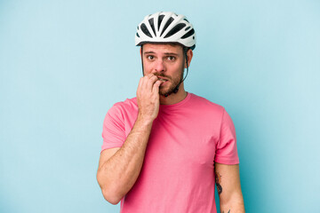 Young caucasian man with bike helmet isolated on blue background biting fingernails, nervous and very anxious.