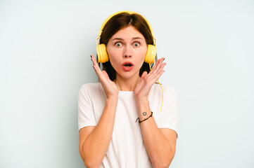 Young English woman listening to music isolated on blue background surprised and shocked.