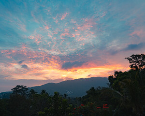 Colorful sunset sky over tress and mountain on a tropical island in a summer evening. View from the top.