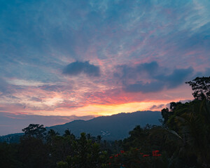 Colorful sunset sky over tress and mountain on a tropical island in a summer evening. View from the top.