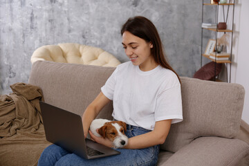 Portrait of young beautiful hipster woman working on a laptop with her adorable wire haired Jack Russel terrier puppy at home. Female with rough coated pup. Interior background, close up, copy space.