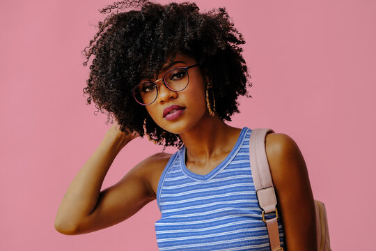beautiful young african american female student in eyeglasses posing on pink background
