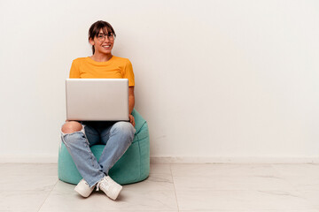 Young Argentinian woman working with pc sitting on a puff isolated on white background happy, smiling and cheerful.