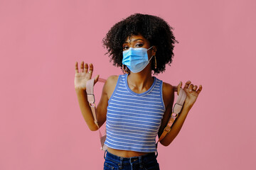 young female student with backpack wearing protective mask and posing on pink background, back to school concept