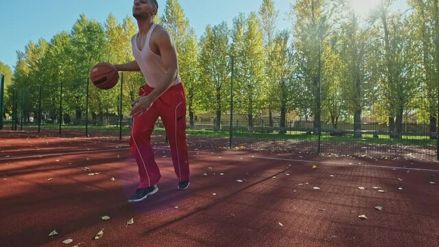 Basketball player training at basketball court in slow motion. Young man practicing ball handling skill at sunny weather. Streetball training in 4K, UHD