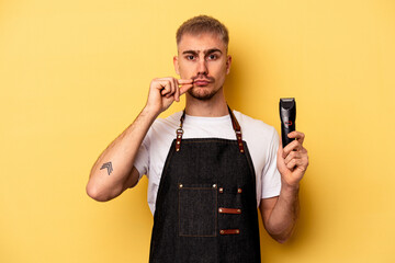 Young caucasian hairdresser man isolated on yellow background with fingers on lips keeping a secret.