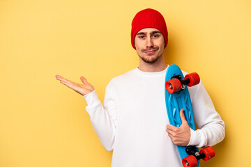 Young skater caucasian man isolated on yellow background showing a copy space on a palm and holding another hand on waist. © Asier