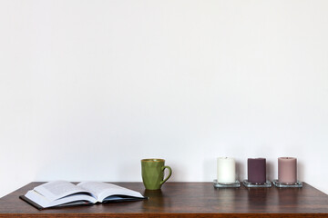Wooden desk with a stack of books. Lifestyle. White wall copy space. An open book. Peaceful mood. Candles.