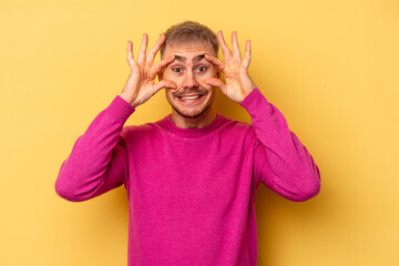 Young caucasian man isolated on yellow background keeping eyes opened to find a success opportunity.