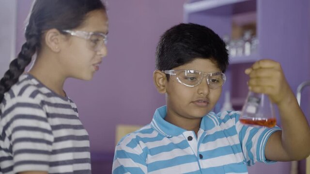 Close up shot of concentreted kids checking or analysing chimical by holding flask while doing experiment at chemistry laboratory