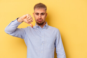 Young caucasian man isolated on yellow background showing thumb down and expressing dislike.