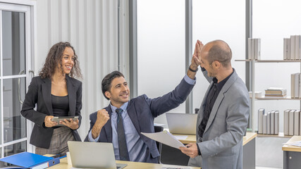 Two male workers give high five to each other to celebrate a project achievement with another female colleague in an office. Co-workers express happiness in team working to meet their business targets