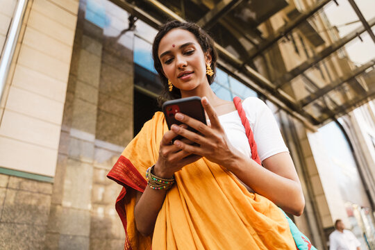 Young Indian Woman Wearing Sari Using Mobile Phone At City Street