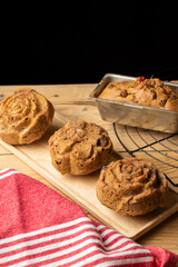 Top view of individual plum cakes on rustic wooden table with red dishcloth, black background, vertical