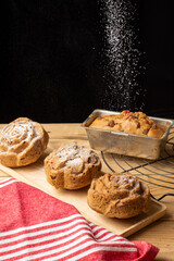 Top view of individual plum cakes with falling sugar, on rustic wooden table with red kitchen cloth, black background, vertical