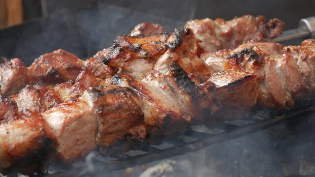 A large fatty juicy pork knuckle is fried on a grill against a background of fire. Street food festival, outdoor picnic