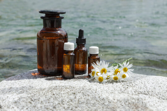 Set of medical bottles against background of water. Bottles on stone and chamomile flowers. Natural medicine.
