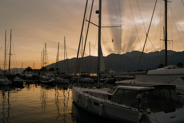Pier with yachts against the background of the rays of the sun setting behind the mountains