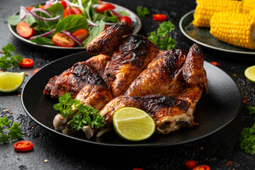 Roast Chicken Tabaka with salad, corn and lime on black plate.