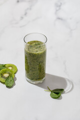 Green smoothie in a glass with slices of kiwi and spinach in the sunlight