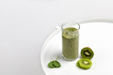 Fototapeta premium Green smoothie in a glass with slices of kiwi and spinach on white round table