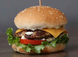 Fresh crispy chicken burger with cheese, tomatoes and lettuce on wood table, American fast food.