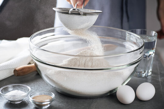 Sifting flour to make dough. Preparing flour to baking bread in kitchen at home.