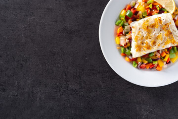 Grilled cod with vegetables in plate on black background. Top view. Copy space