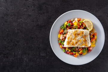 Grilled cod with vegetables in plate on black background. Top view. Copy space