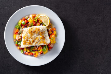 Grilled cod with vegetables in plate on black background. Top view. Copy space