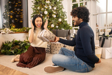 Obraz premium Man giving gift to enthusiastic woman sitting on floor