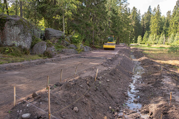 The excavator digs a trench for laying a storm drain and a grid for strengthening the slopes of the mountain at a construction site in a forested area. Construction of a road, drainage ditch and drain