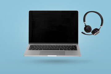 Laptop computer with empty screen and headset  levitating in the air on a bright blue background.