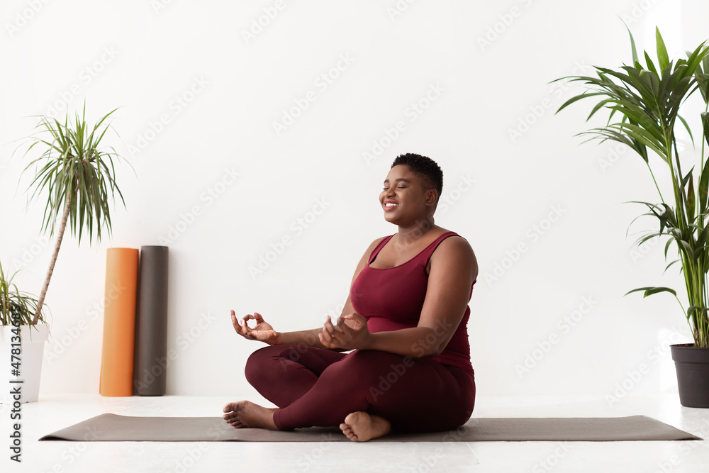 Wall mural Positive fat black lady in sportswear having yoga practice