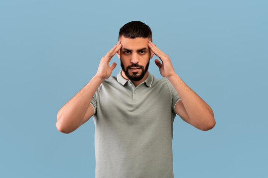 Middle eastern man suffering from headache, massaging temples to get rid of pain, standing over blue background