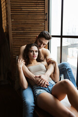 portrait of a charming young couple at home. man is embracing his girlfriend near window. Two people relaxing together