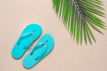 Blue flip flops and decorative palm leaves on a beige paper background. Summer vacation and travel concept. Creative layout. Top view, flat lay.