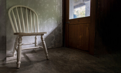 One white wooden vintage chair standing in an empty room under the light from the door. Space for text, Selective focus.