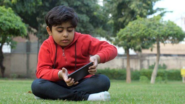 A  little kid playing a video game - lost game and unhappy  screen addiction  video game addiction. A young boy in casual clothes using a mobile while sitting outdoors - leisure time  electronic ga...