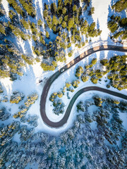 Aerial top down view of a winter landscape with snow covered fir trees and the slopes of a road leading down the mountain