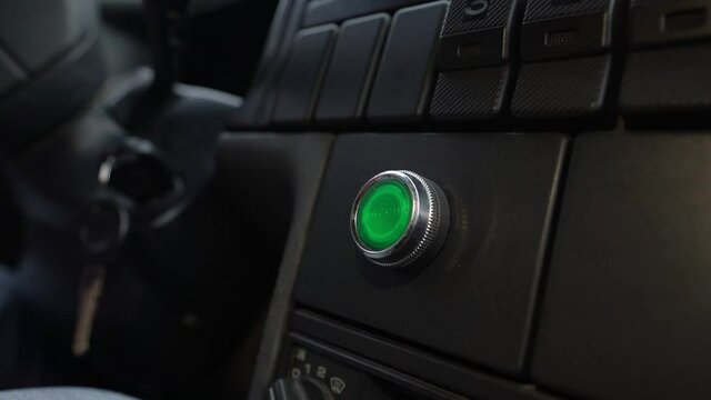Pushing green power ignition button to start keyless car engine. Driver finger pressing starting system.