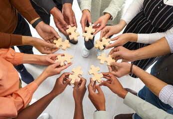 Business and cooperation. Multiracial people stand in circle and connect wooden pieces of puzzles...