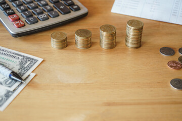 Stack of gold money coin on wood desk with calculator, pen, bank book and money with copy space. 