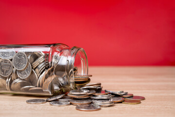 Close up of coins spilling from a money jar on table with red background.