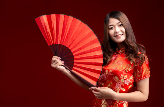 Young Asian woman in chinese traditional cheongsam qipao dress holding fan isolated on red background. Chinese new year concept